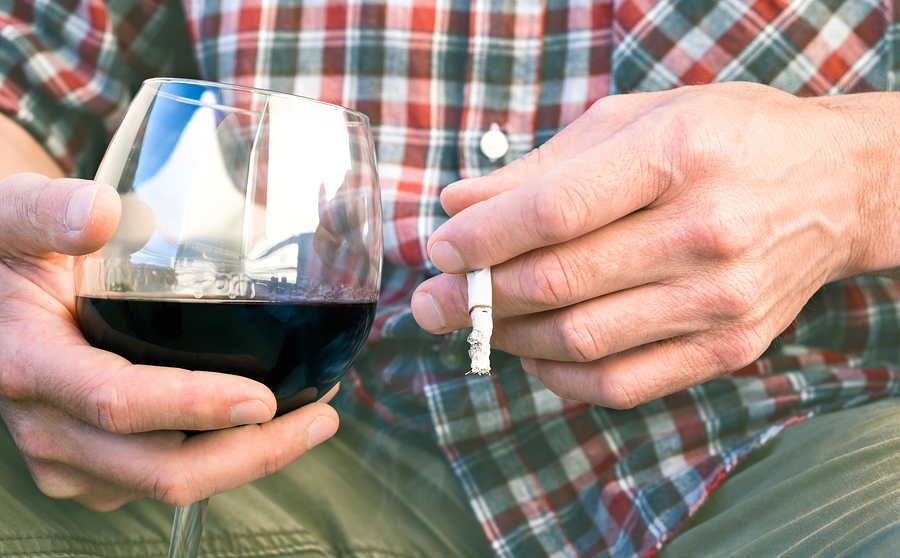 Person drinking a glass of red wine and smoking a cigarette.